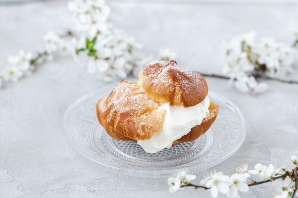 Choux Bun with whipped cream and sugar powder on top. Choux pastry dessert. French cream puff